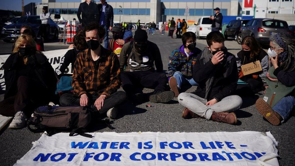 A group of environmentalists sitting on the ground with a banner that reads "Water is the source of life, not for companies to consume" on the day of delivery.